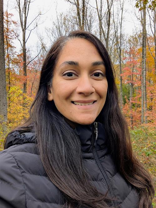 Smiling woman standing in a forest of vibrant autumn maple trees