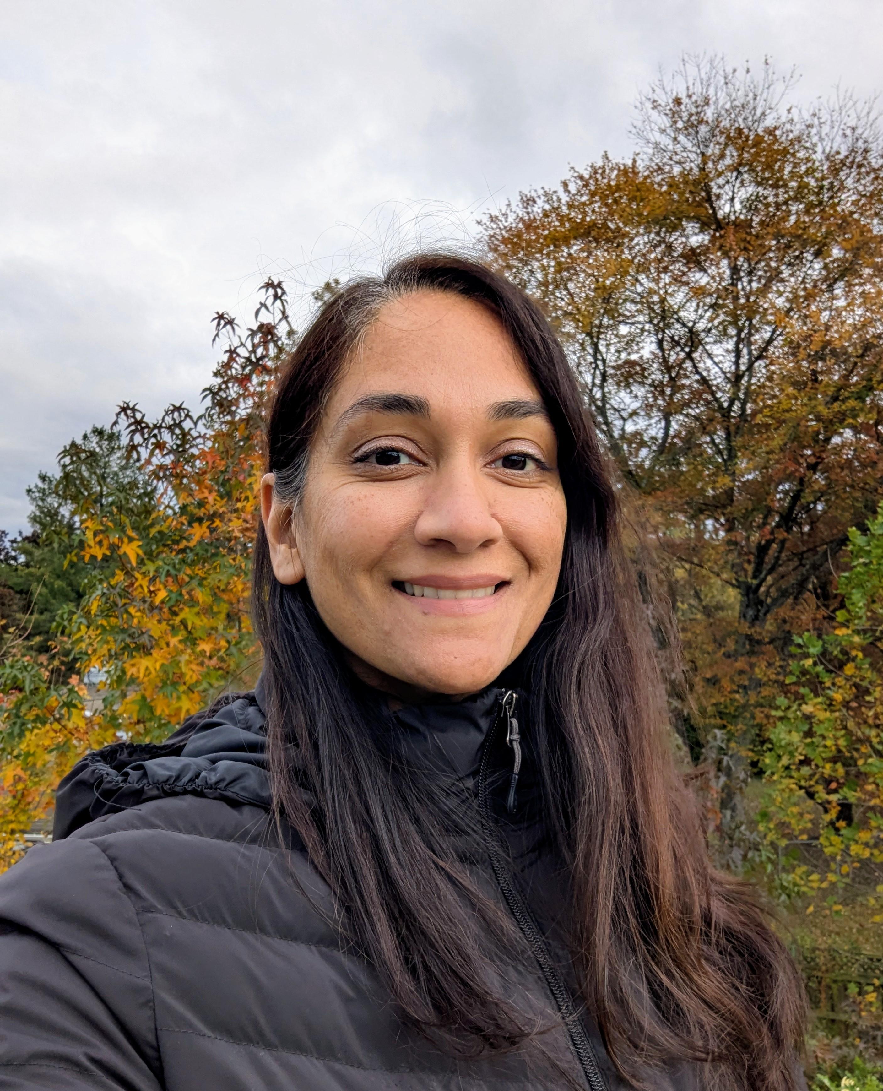 Smiling woman standing in a forest of vibrant autumn maple trees